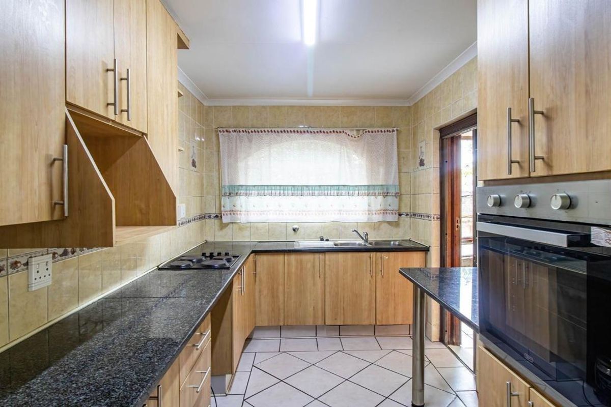 Functional kitchen featuring light wood-look cabinetry, dark granite countertops, built-in oven, and hob, with tiled flooring and backsplash.