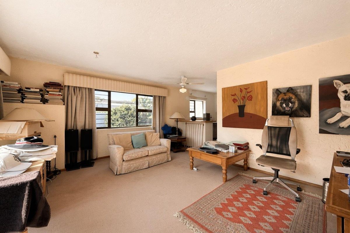 A spacious living room featuring neutral wall finishes, carpeted flooring, a ceiling fan, and large windows that provide natural light.