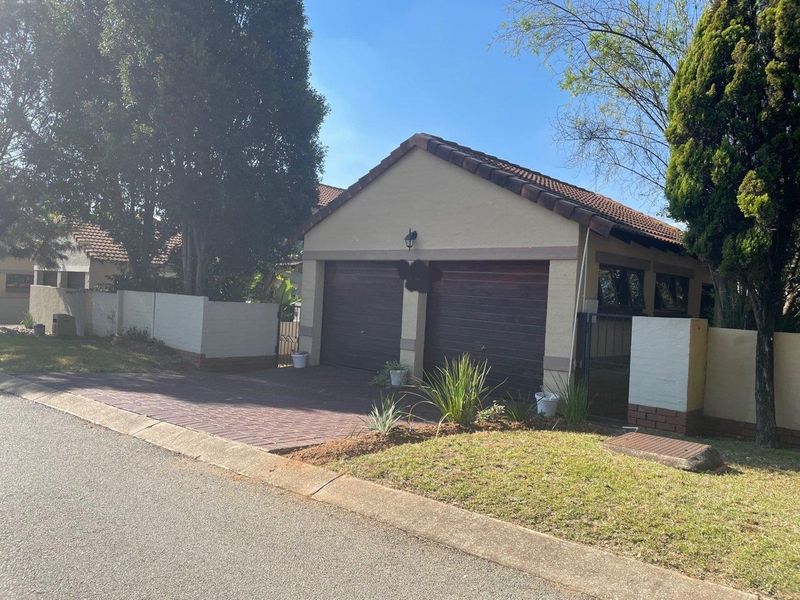 Front view of the property featuring a double garage with wooden doors, a paved driveway, and a well-maintained boundary wall.
