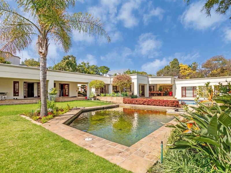 A spacious rear garden featuring a central swimming pool, manicured lawn, and direct access to the home via multiple sets of french doors.