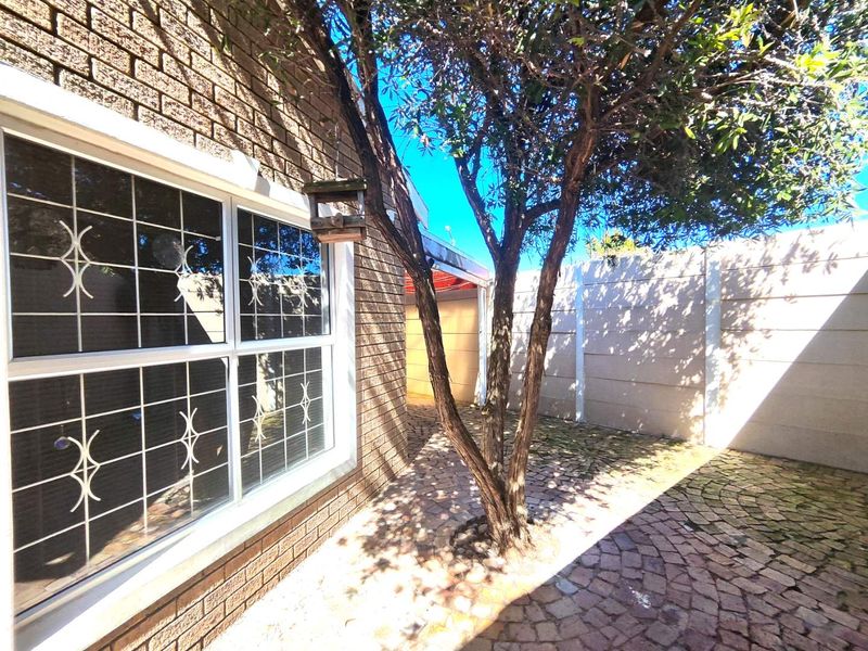A private rear courtyard featuring brick exterior walls, security-barred windows, and paved flooring enclosed by a precast concrete boundary wall.