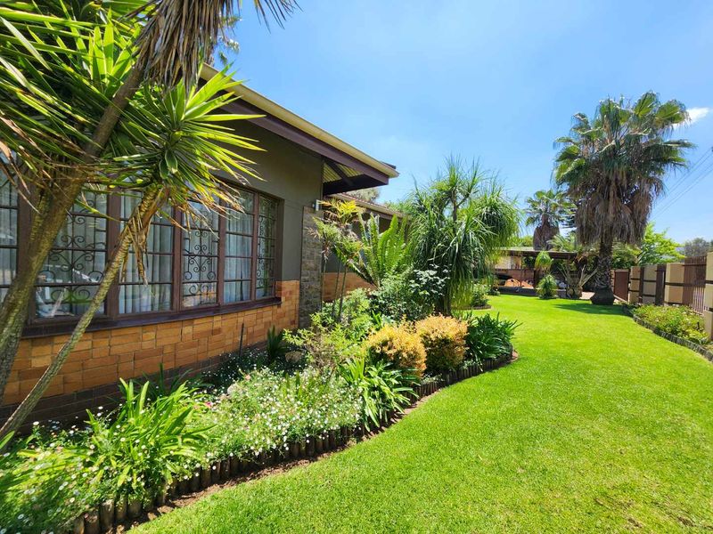 A well-maintained rear garden featuring a lush green lawn, established landscaping, and a brick-clad house exterior with timber-framed windows.