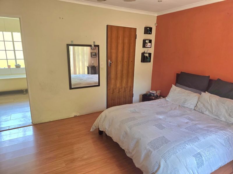 A bedroom featuring laminate flooring, a wooden door, and an accent wall, with an adjoining bathroom visible through the doorway.