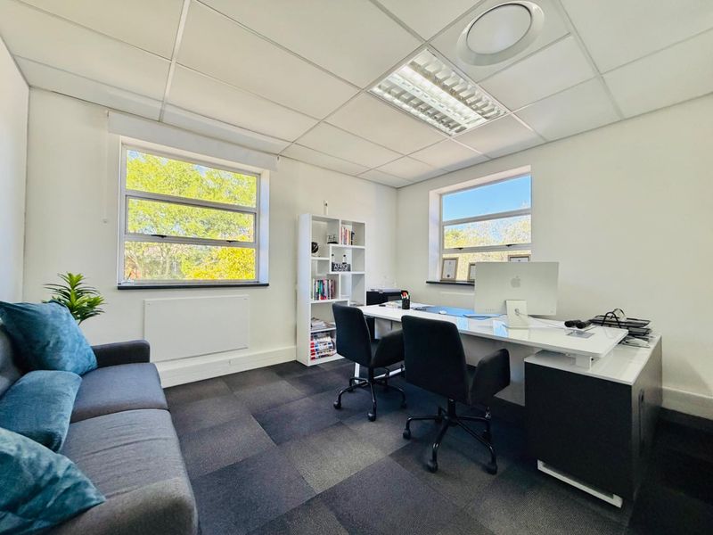 A bright and functional office space featuring carpet tiles, suspended ceilings with recessed lighting, and large windows providing natural light.