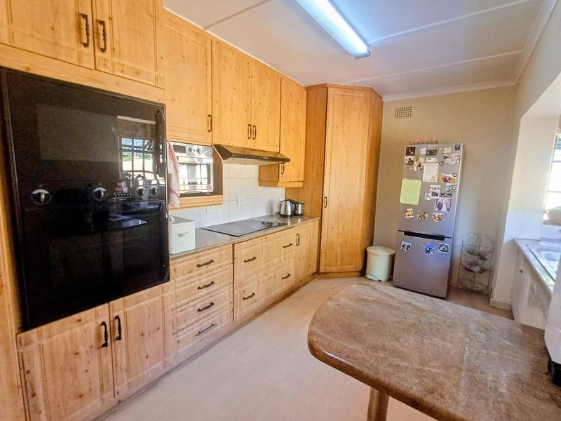 A functional kitchen featuring extensive wooden cabinetry, built-in oven and microwave, electric hob, and laminate countertops with a tiled backsplash.