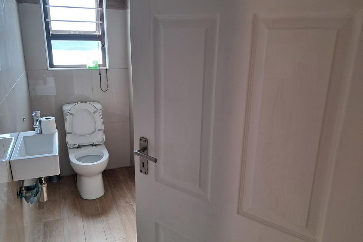 A compact, functional bathroom featuring a wall-mounted basin, toilet, and neutral tiled finishes.