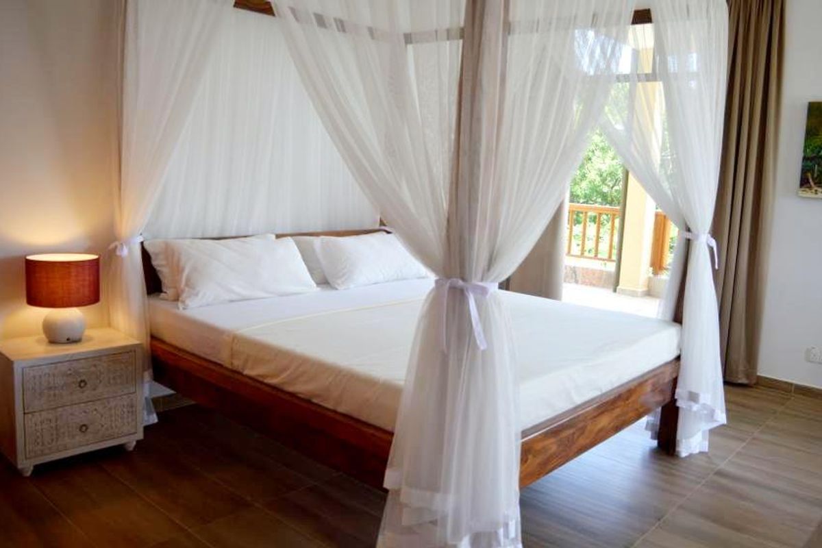 A bright bedroom featuring wood-look tile flooring and direct access to a private balcony through large glass sliding doors.