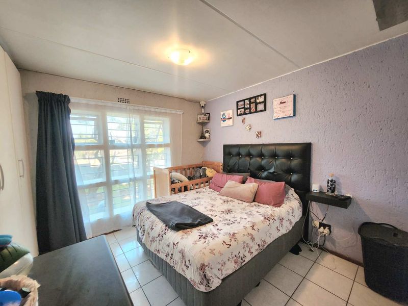 A bedroom featuring tiled flooring, a built-in wardrobe, and a window with security bars, offering a functional space with potential for cosmetic updates.