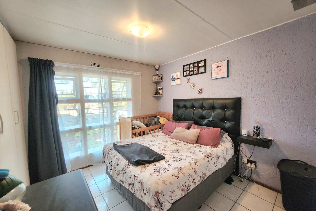 A bedroom featuring tiled flooring, a built-in wardrobe, and a window with security bars, offering a functional space with potential for cosmetic updates.