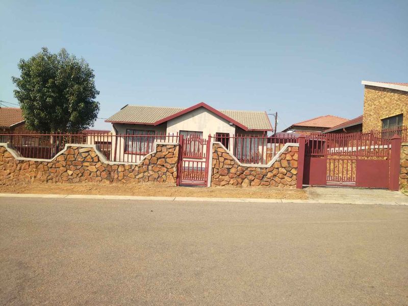 Front elevation of a residential house featuring a stone-clad boundary wall, metal security fencing, and gated access from the street.
