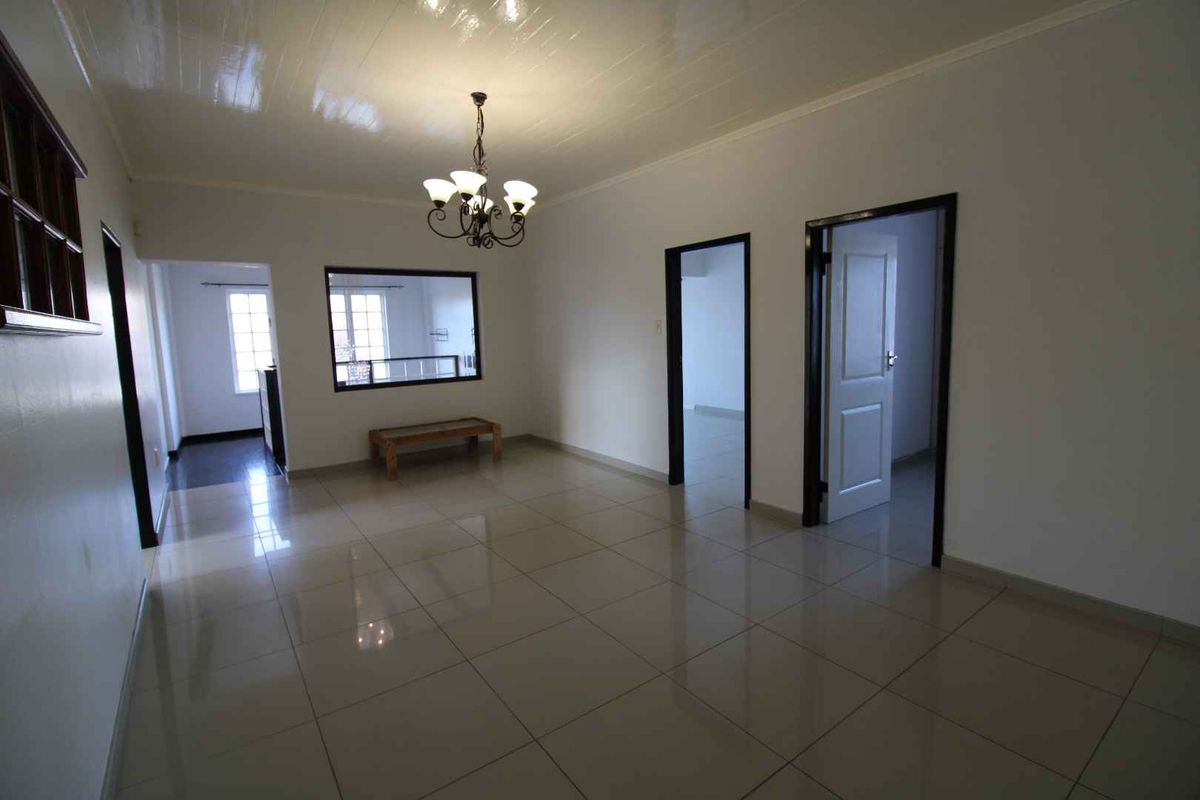 A spacious, tiled living area featuring a central chandelier, neutral walls, and multiple doorways leading to adjacent rooms.