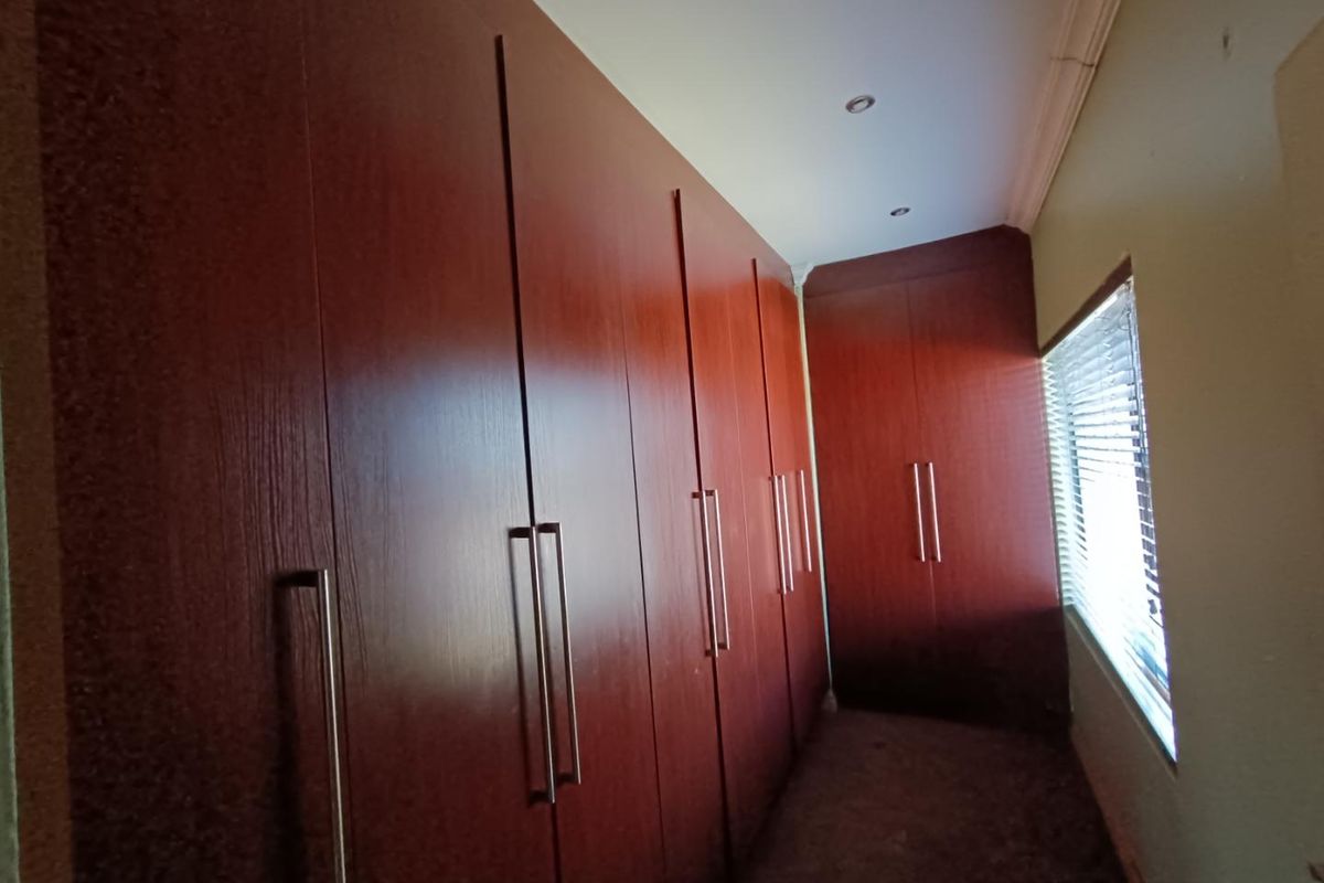 A bedroom featuring extensive floor-to-ceiling built-in wooden cabinetry with modern handles and a window fitted with horizontal blinds.
