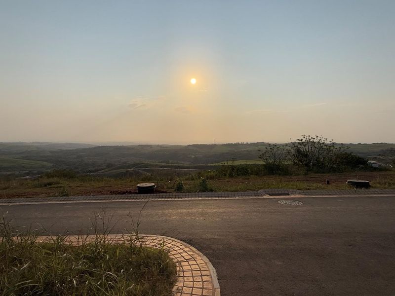 A scenic view overlooking the surrounding landscape from a paved residential street, featuring clear horizon lines and established road infrastructure.