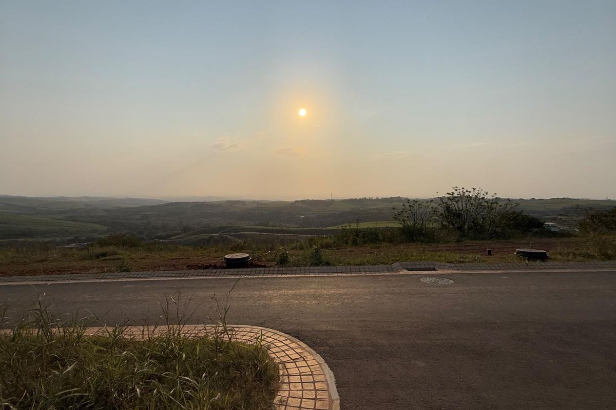 A scenic view overlooking the surrounding landscape from a paved residential street, featuring clear horizon lines and established road infrastructure.