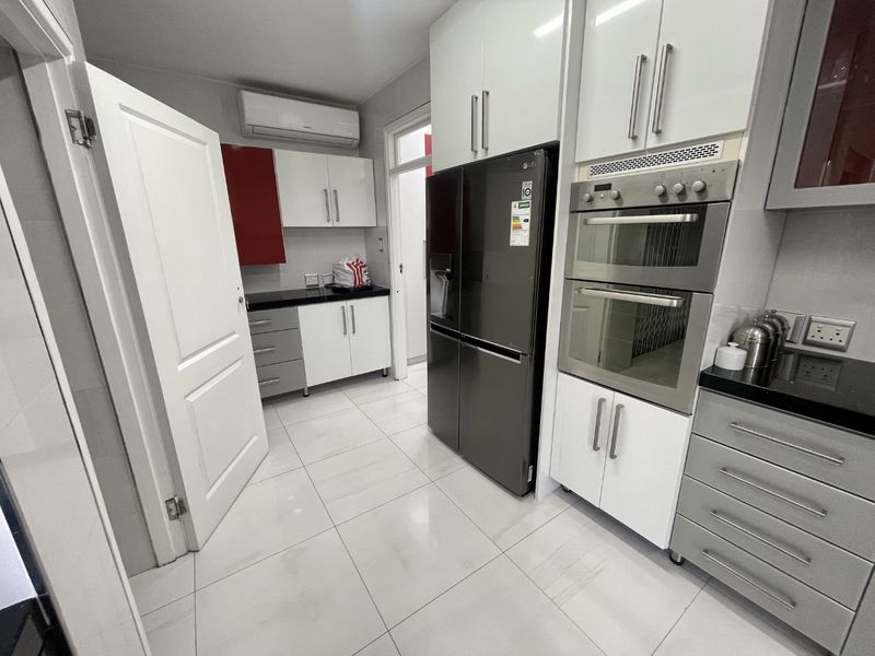 Modern kitchen featuring high-gloss cabinetry, granite countertops, a double wall oven, and tiled flooring, providing a clean and functional culinary space.