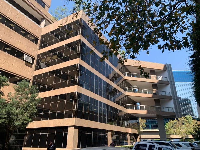A modern multi-story office building featuring a glass curtain wall facade, stone cladding, and integrated balconies with metal railings.