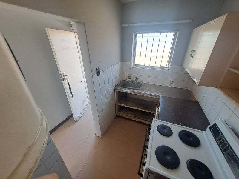 A compact kitchen featuring a stainless steel sink, tiled splashback, and electric stove, requiring cosmetic updates and repairs to cabinetry and finishes.