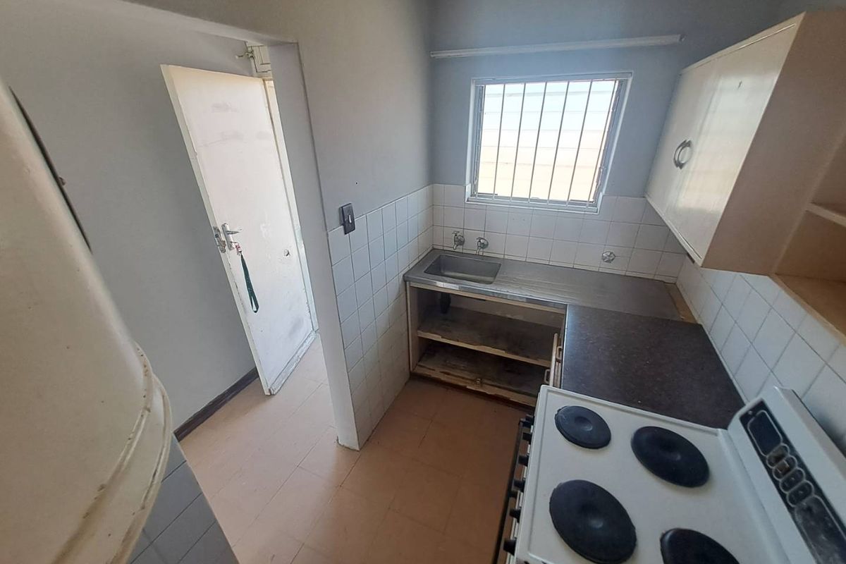 A compact kitchen featuring a stainless steel sink, tiled splashback, and electric stove, requiring cosmetic updates and repairs to cabinetry and finishes.