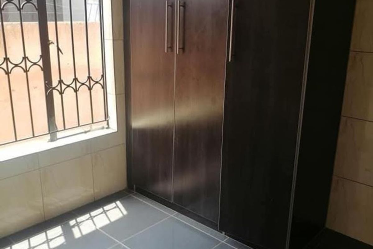 A clean, empty bedroom featuring dark wood built-in wardrobes, tiled flooring, and a window fitted with security bars.