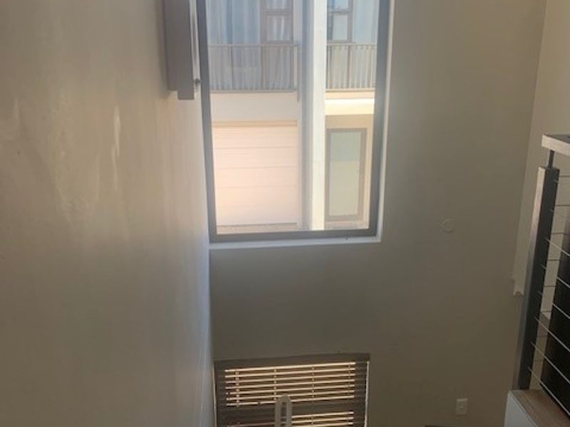 A bright, modern staircase area featuring a large window, wooden treads, and a contemporary metal balustrade.