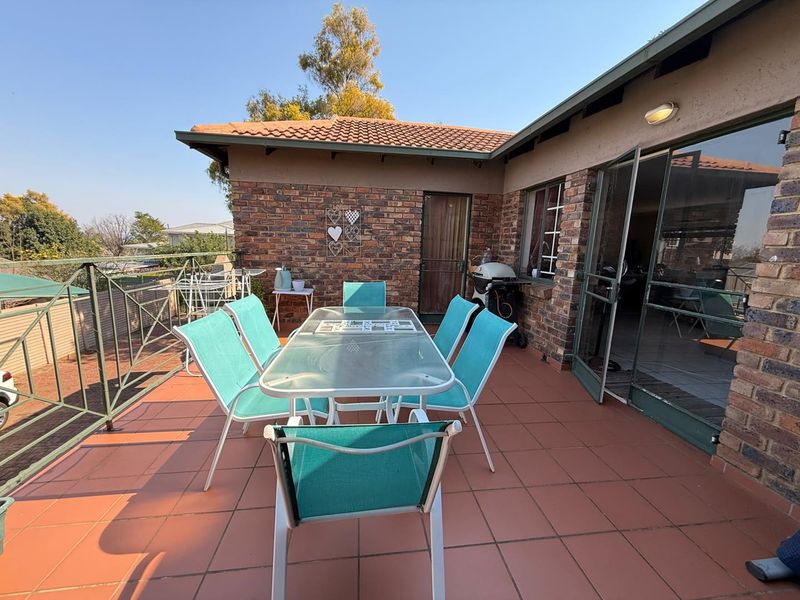 An elevated outdoor patio featuring tiled flooring, brick wall finishes, and metal railings, providing direct access to the interior through sliding glass doors.