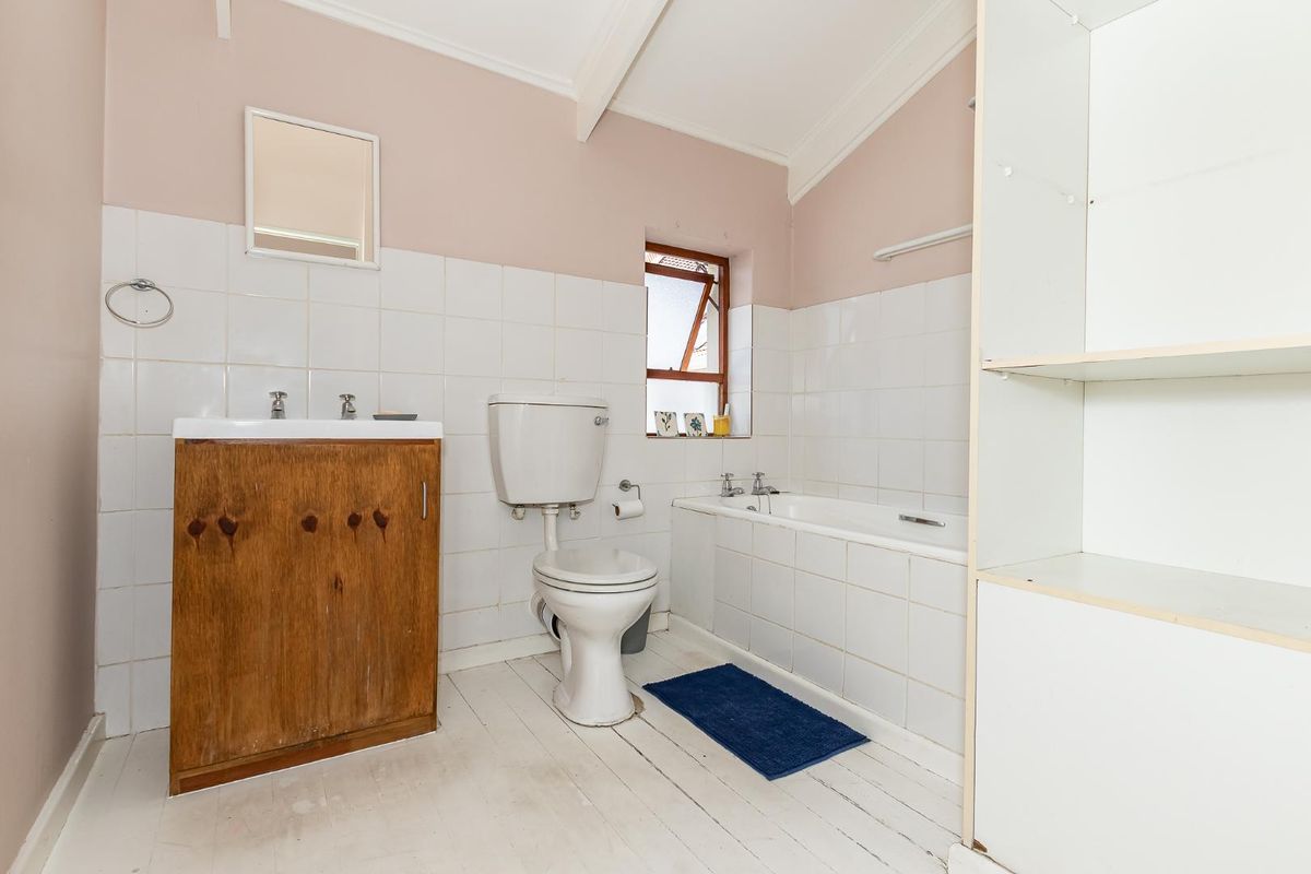 A dated bathroom featuring a built-in bathtub, a toilet, and a wooden vanity cabinet with a wall-mounted mirror and tiled splashback.
