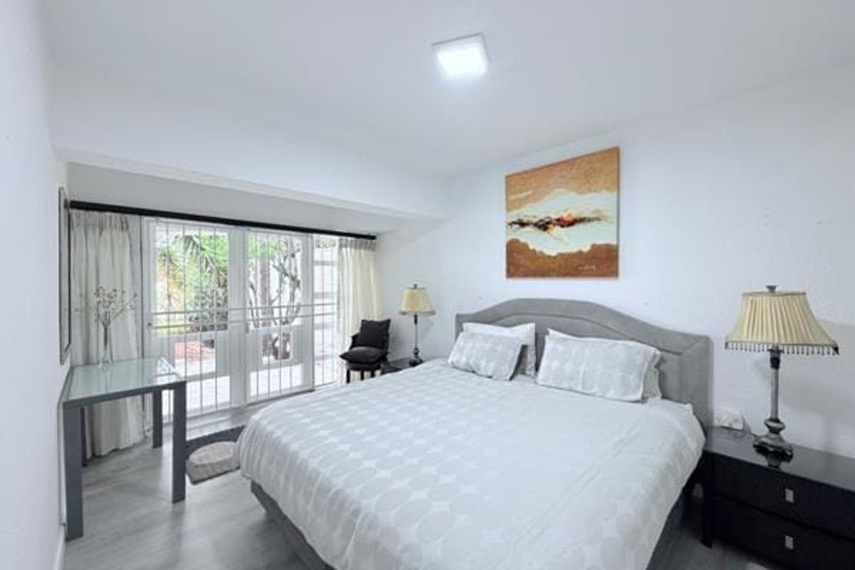 A well-lit bedroom featuring laminate flooring and a sliding glass door with a security gate, providing direct access to the outdoor area.