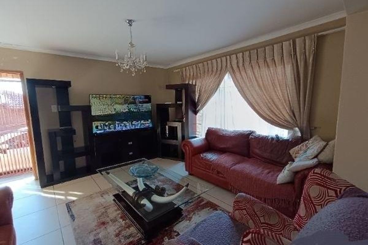 A living room featuring tiled flooring and a central chandelier, with large windows dressed in full-length curtains.