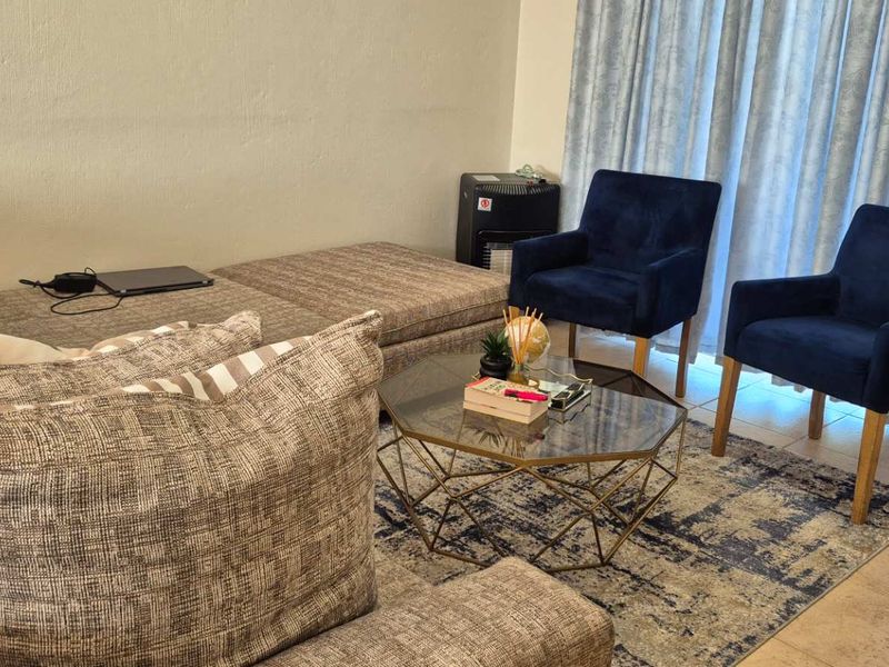A comfortable living room area featuring tiled flooring and large windows with curtains, providing a functional and inviting space for relaxation.
