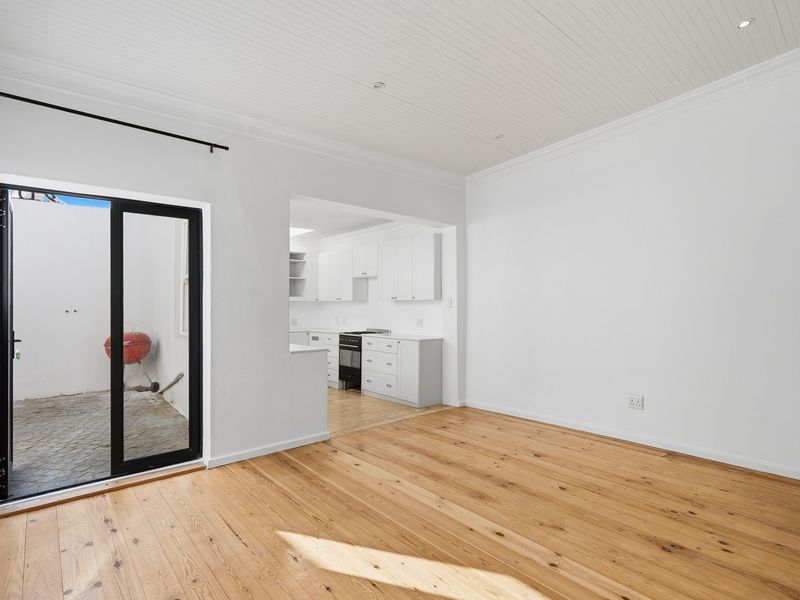 Bright open-plan living area featuring polished timber flooring, tongue and groove ceilings, and a seamless transition to a modern kitchen and private courtyard.