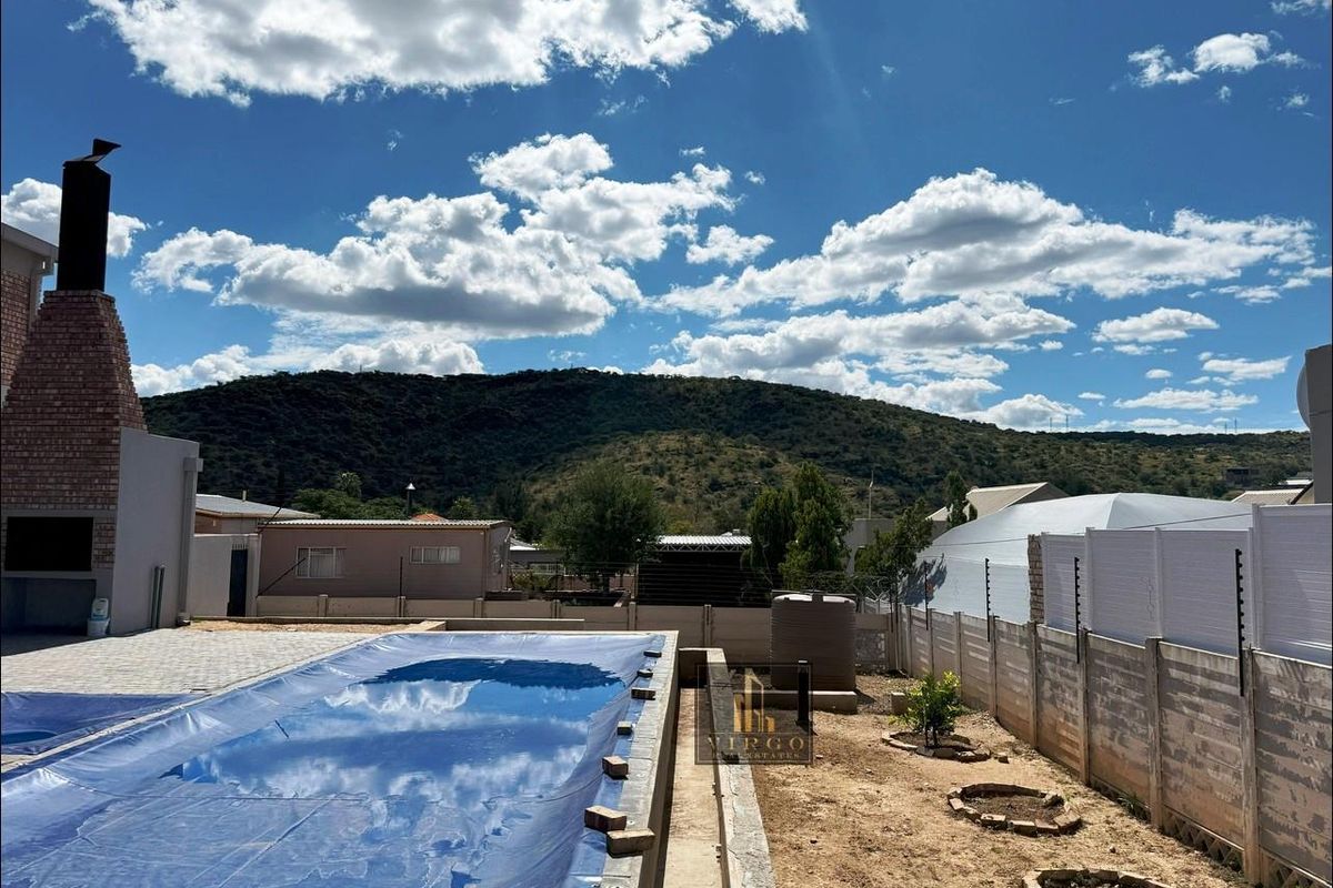 Outdoor pool area featuring a built-in braai, covered swimming pool, and mountain views, enclosed by precast walling with electric fencing.