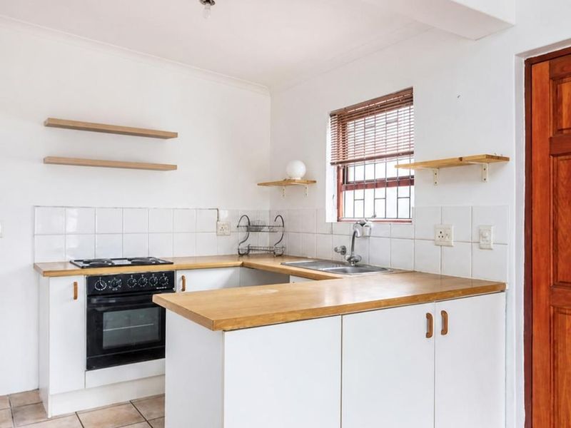 A functional kitchen featuring wooden countertops, built-in oven with gas hob, tiled splashback, and ample storage cabinetry in a clean, neutral space.