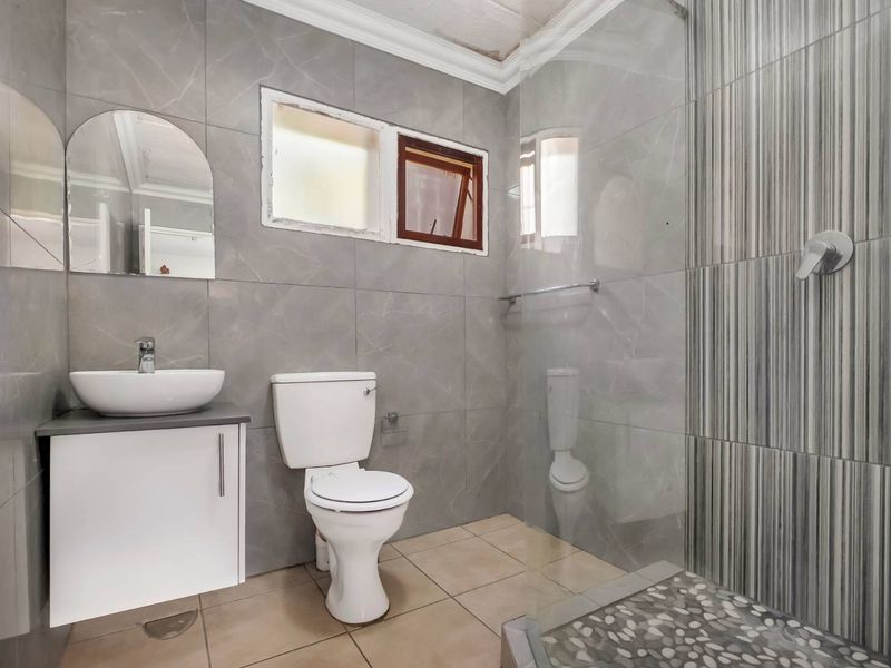 Modern bathroom featuring grey wall tiles, a vessel sink with vanity, a toilet, and a walk-in shower with a pebble floor.