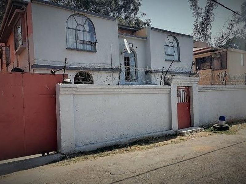 Front exterior view of a two-story house featuring a perimeter wall with security razor wire, arched windows, and a gated entrance.