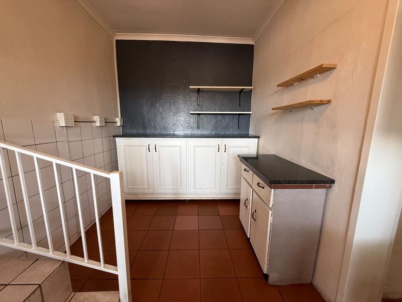 A functional scullery or utility area featuring built-in white cabinetry, dark stone countertops, tiled splashbacks, and open shelving, located adjacent to a staircase.
