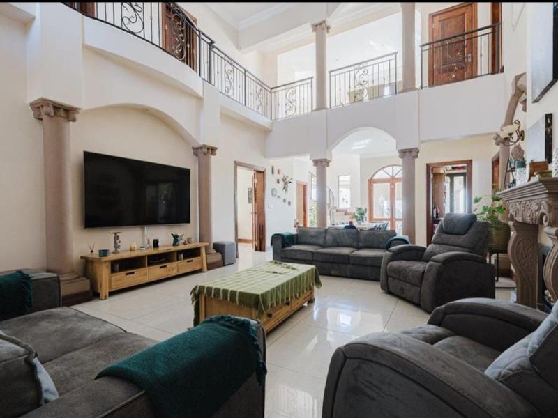Spacious double-volume living room featuring elegant architectural columns, a stone fireplace, and a mezzanine balcony with decorative wrought iron railings.