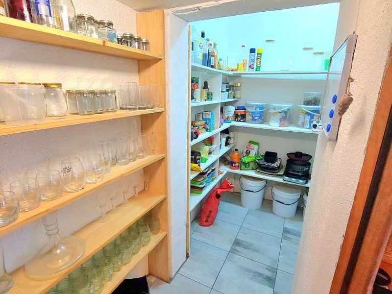 A functional scullery or pantry area featuring extensive built-in shelving and durable tiled flooring, providing ample storage space.
