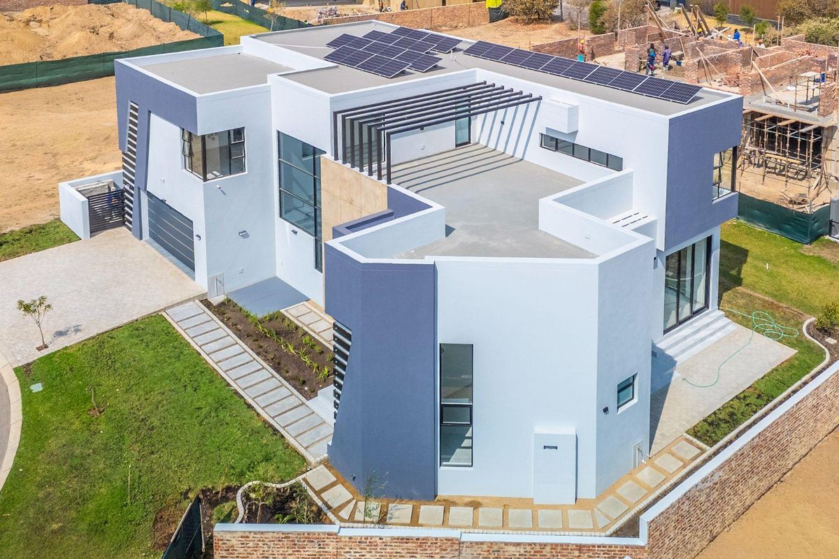 Aerial view of a modern double-story residence featuring a flat roof with solar panels, a pergola, and a paved driveway in a developing estate.