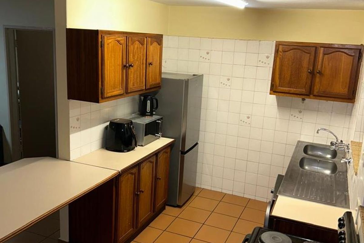 A functional kitchen featuring wooden cabinetry, tiled splashbacks, a freestanding stove, and a stainless steel sink, offering a practical layout for daily meal preparation.