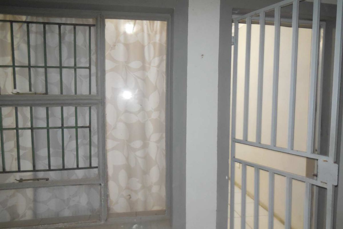 A view of a window with security bars and a metal security gate, showing signs of wear on the surrounding wall and frames.