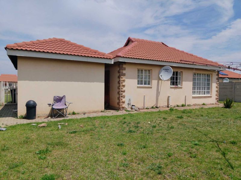 Rear view of a single-story residential house featuring a tiled roof, plastered walls, and a surrounding lawn area.