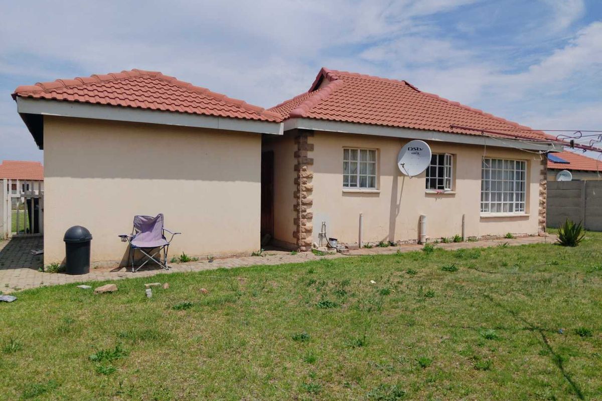Rear view of a single-story residential house featuring a tiled roof, plastered walls, and a surrounding lawn area.