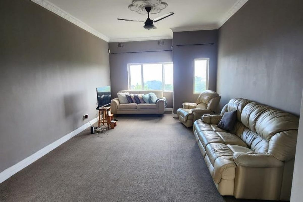 Spacious living room featuring neutral wall tones, carpeted flooring, decorative ceiling rose with fan, and ample natural light from multiple windows.
