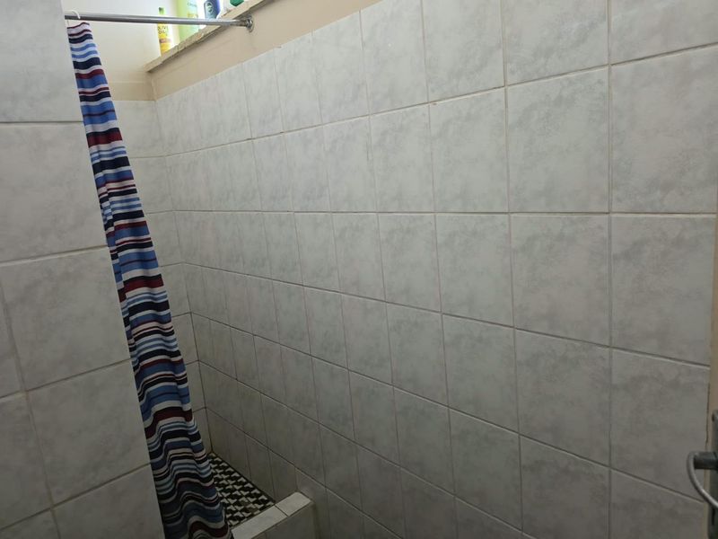 A functional bathroom shower area featuring tiled walls and flooring, currently equipped with a shower curtain rod.