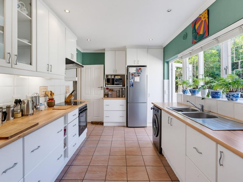 A functional kitchen featuring white cabinetry, wooden countertops, a double basin sink, and integrated appliances, with direct access to the garden.
