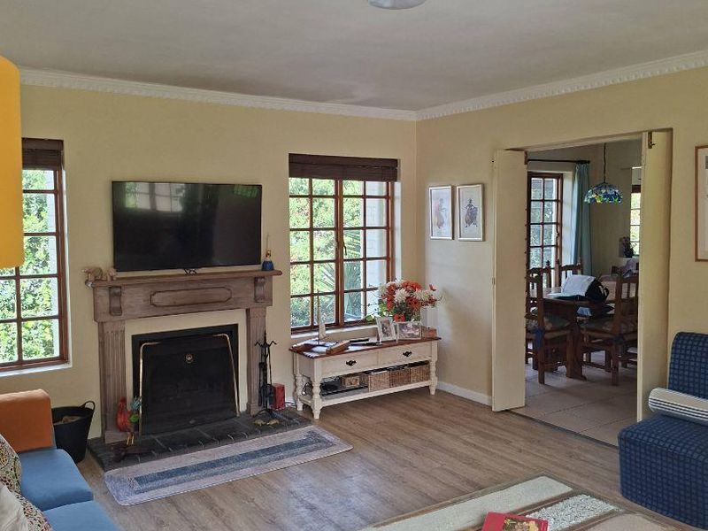 A comfortable living room featuring a traditional fireplace with a wooden mantelpiece, timber-framed windows, and crown molding, with an adjacent dining area visible.