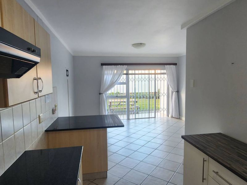 Open-plan kitchen and living area featuring tiled floors, built-in cabinetry with dark countertops, and a sliding door leading to an outdoor space.