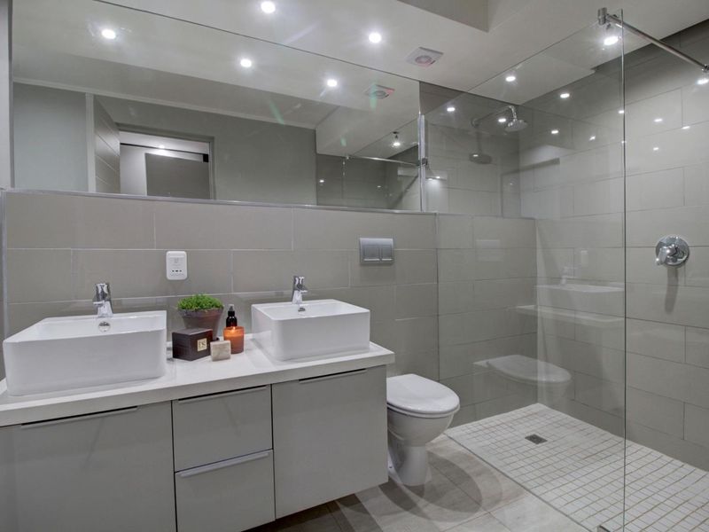 Modern bathroom featuring a double vanity, wall-mounted toilet, and a spacious walk-in shower with a glass screen and contemporary tiled finishes.