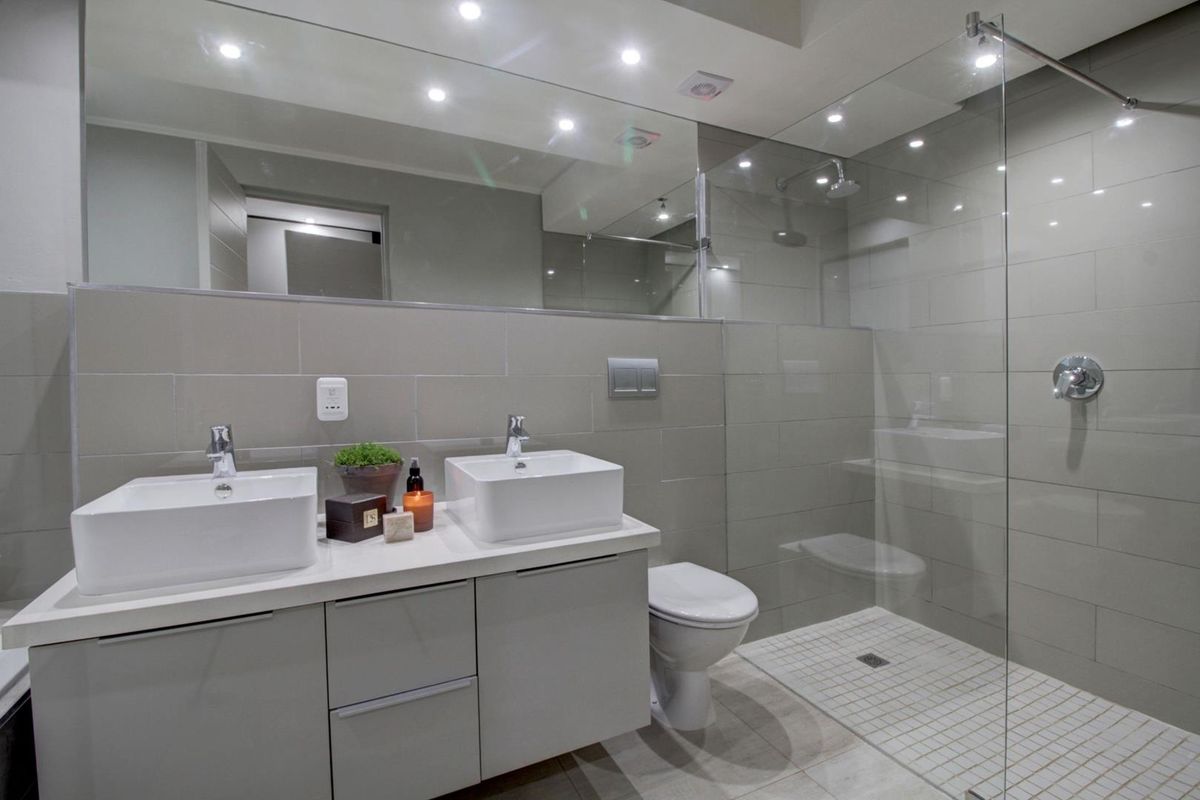 Modern bathroom featuring a double vanity, wall-mounted toilet, and a spacious walk-in shower with a glass screen and contemporary tiled finishes.