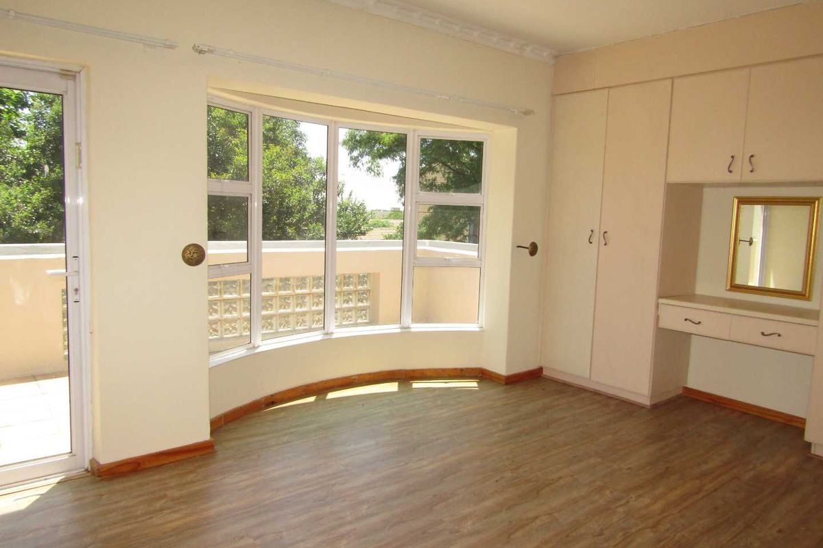 A bright bedroom featuring a large bay window, built-in vanity and wardrobe cabinetry, and direct access to an outdoor balcony area.